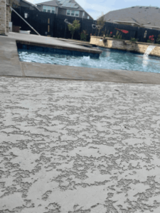Textured concrete beside swimming pool in backyard.