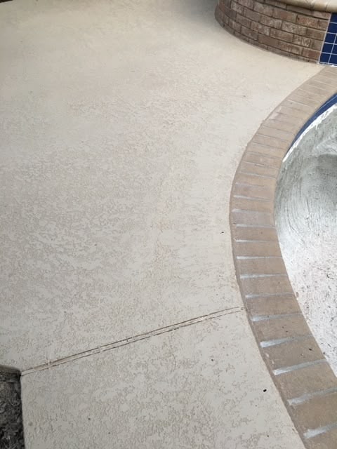 Textured concrete pool deck with brick edging.