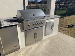 Outdoor kitchen with grill and refrigerator.