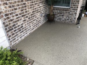 Textured concrete patio with brick wall and plants.