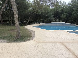 Outdoor pool surrounded by trees and concrete patio