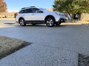 White SUV parked on driveway with trees nearby.