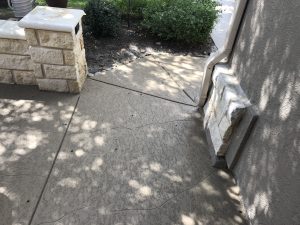 Textured concrete path beside brick wall and plants.