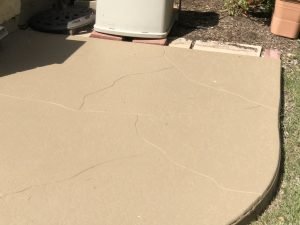Cracked beige concrete patio beside garden.