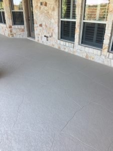 Textured concrete patio beside stone house exterior.